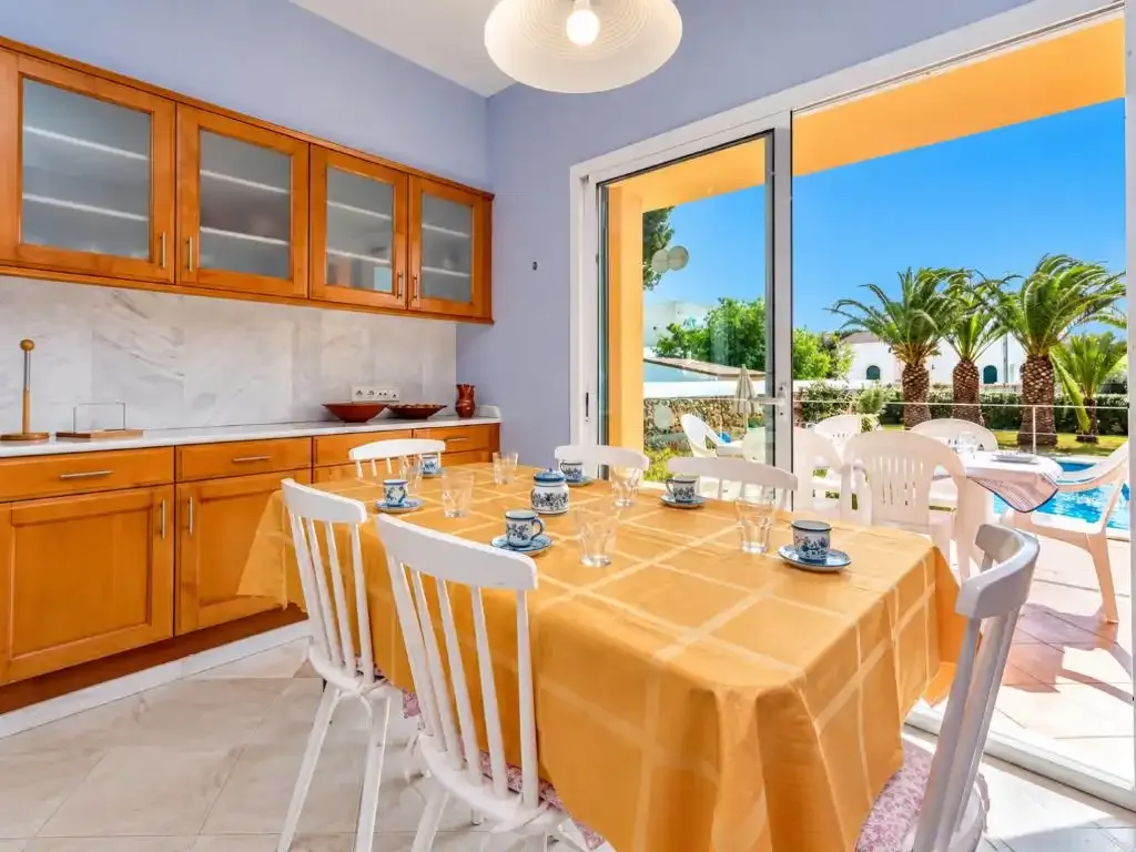 Comedor con la mesa puesta junto a grandes puertas de vidrio que dan a un patio con piscina.