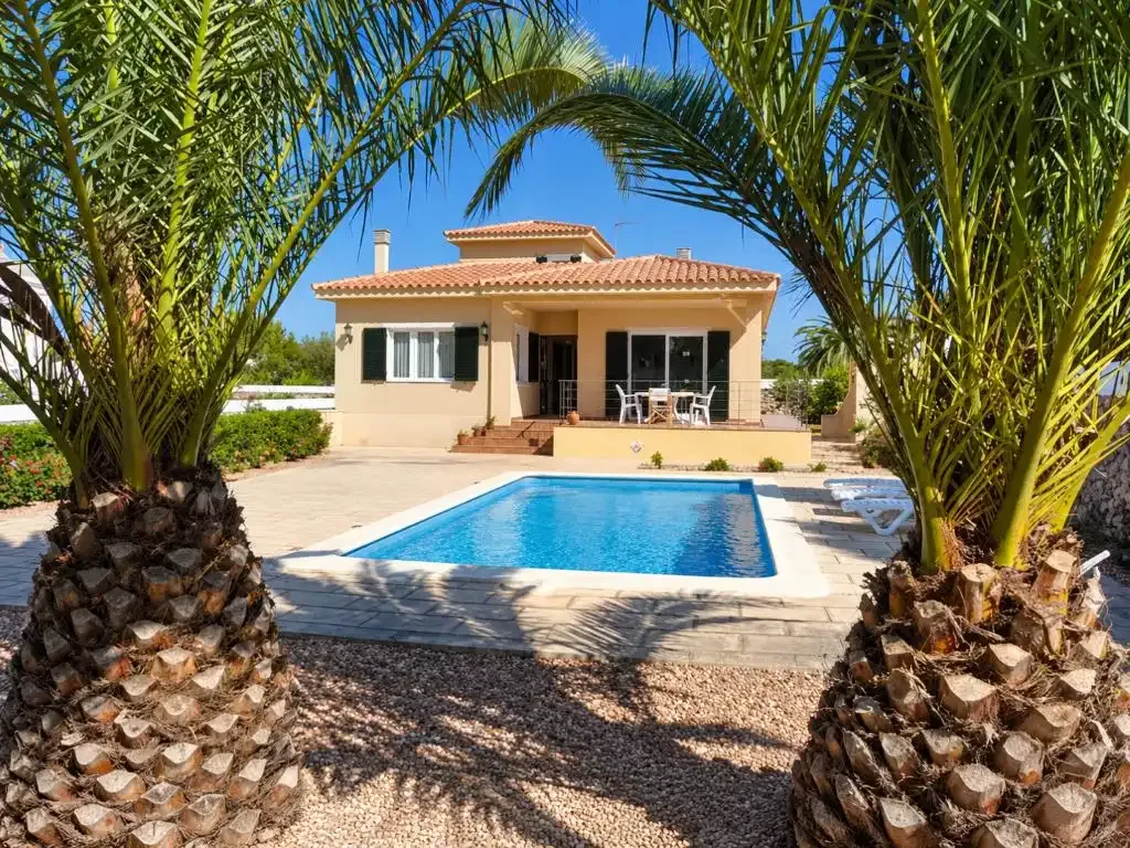 Una casa está detrás de una piscina rectangular, enmarcada por palmeras.