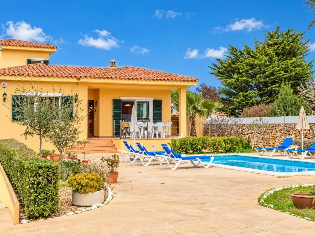 Una casa amarilla da a un patio con piscina y tumbonas.