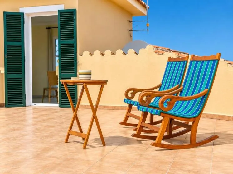 Una terraza embaldosada con dos sillones a rayas junto a una puerta abierta.