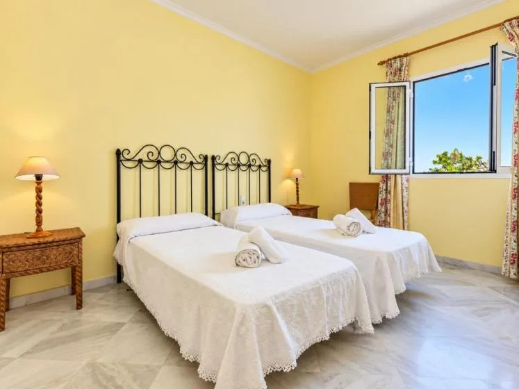 Un dormitorio luminoso con dos camas y una ventana abierta.