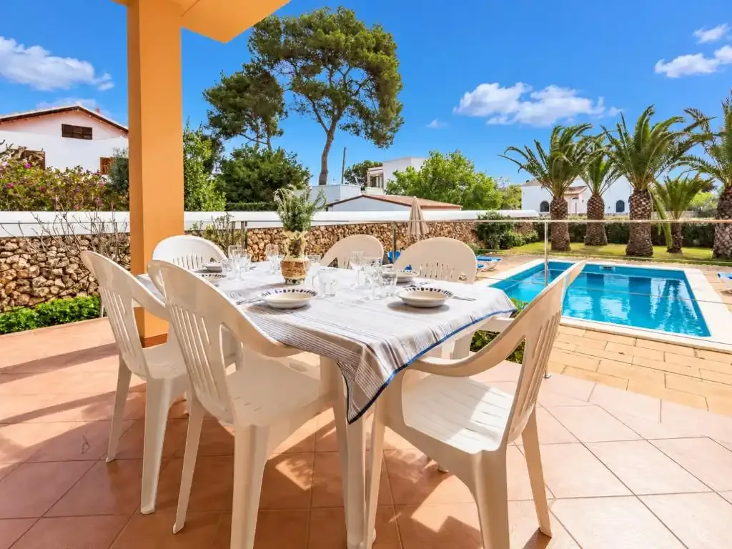 Una zona de comedor en el patio da a una piscina y a unas palmeras.