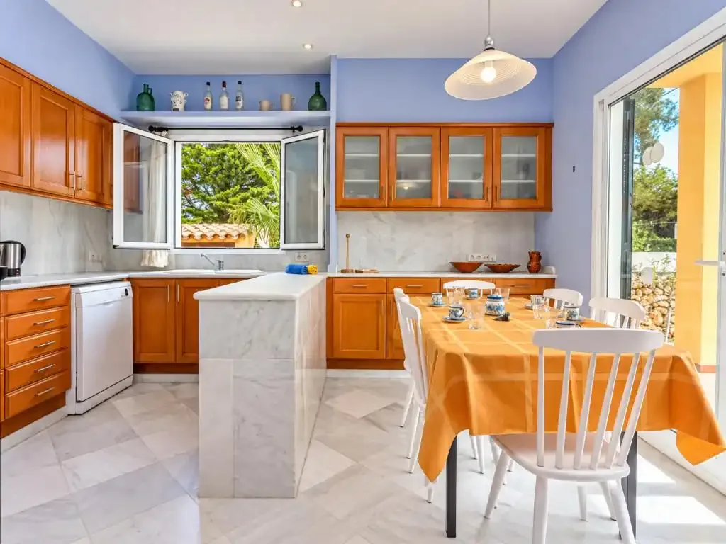Una cocina luminosa con zona de comedor, armarios de madera y una mesa.