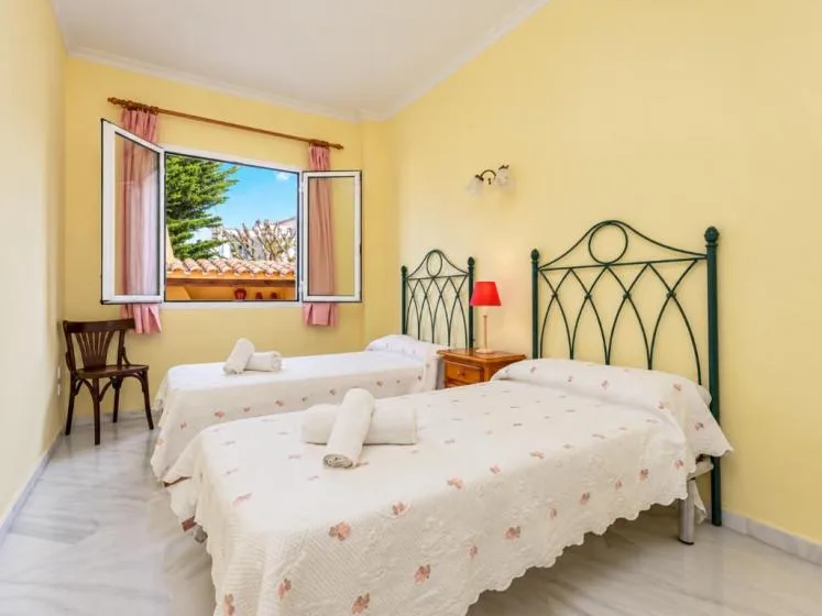 Un dormitorio amarillo con dos camas y una ventana abierta con vistas a los árboles.
