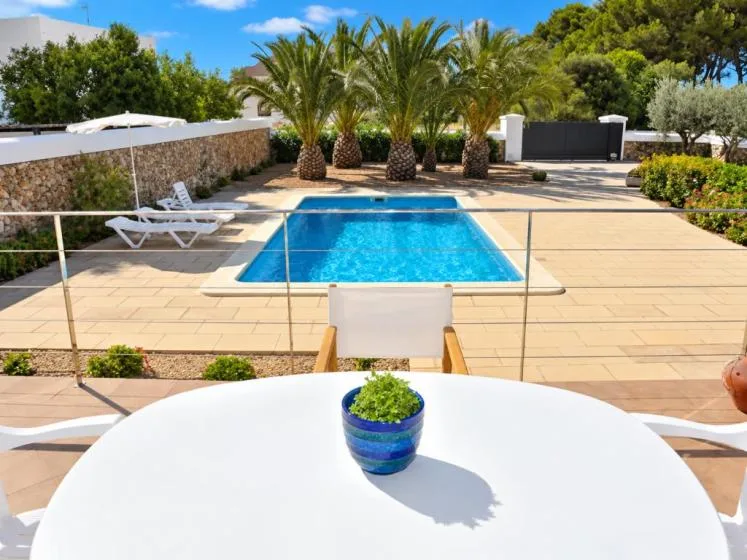 Una piscina está en un patio soleado pavimentado con palmeras.