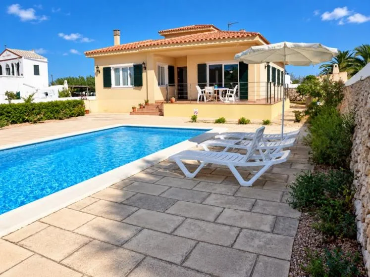 Una casa da a una piscina con asientos reclinables en el patio pavimentado.
