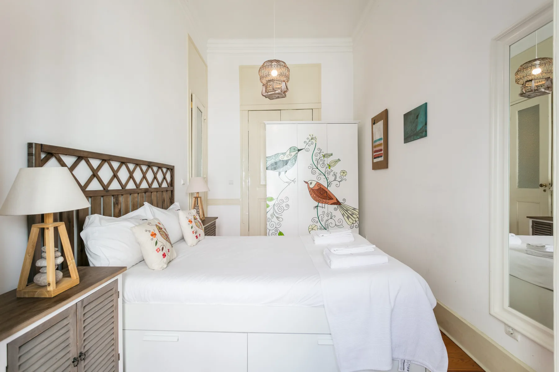 A bedroom with a neatly made bed and bird illustrations on a folding screen.