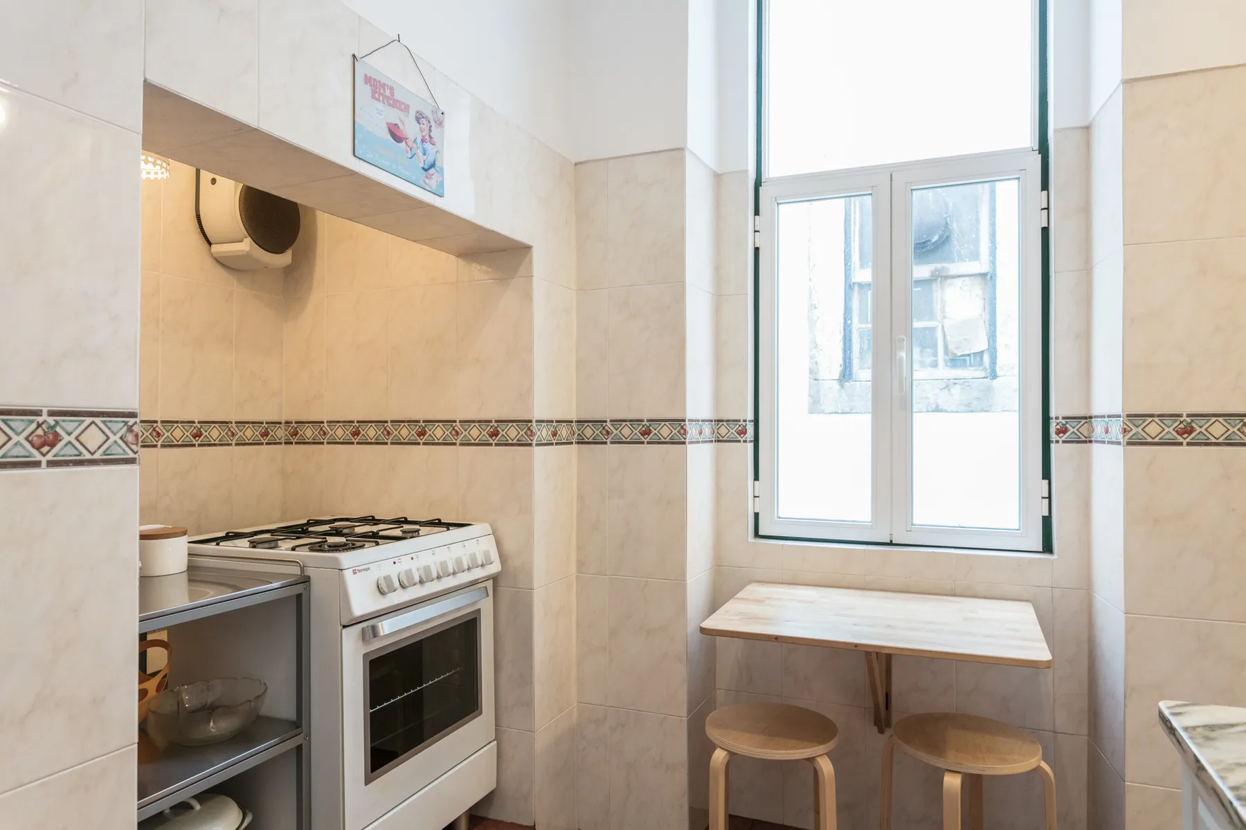 A tiled kitchen with a stove, a window, and a small table with stools.