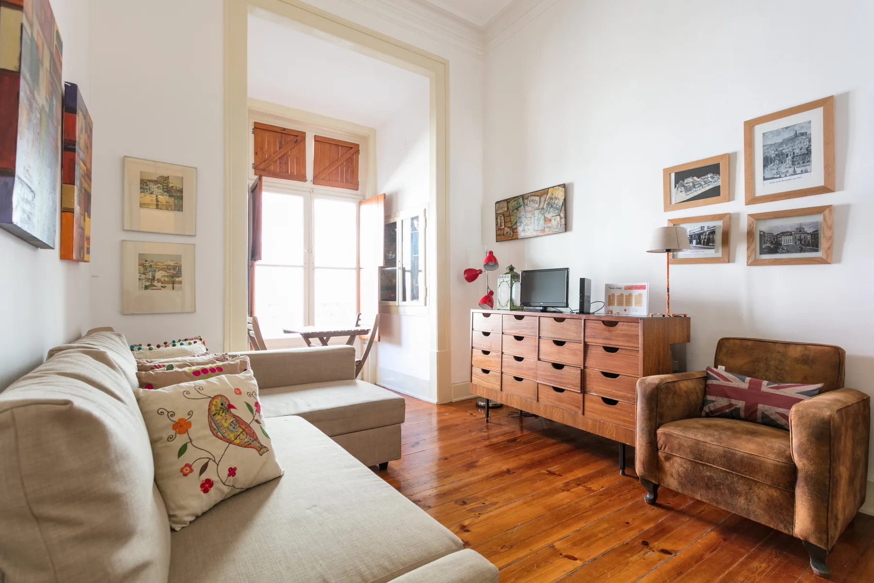 A bright living room with seating, a wooden dresser, and framed pictures.