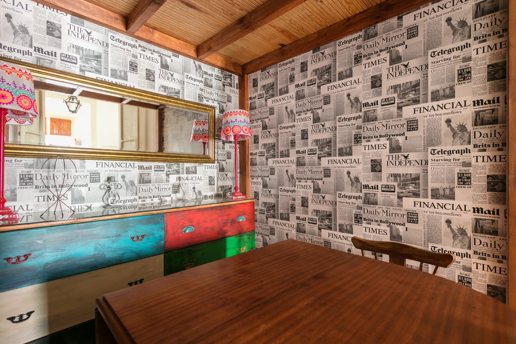 A dining area with a wooden table, colorful built-in seating, and newspaper-print walls.