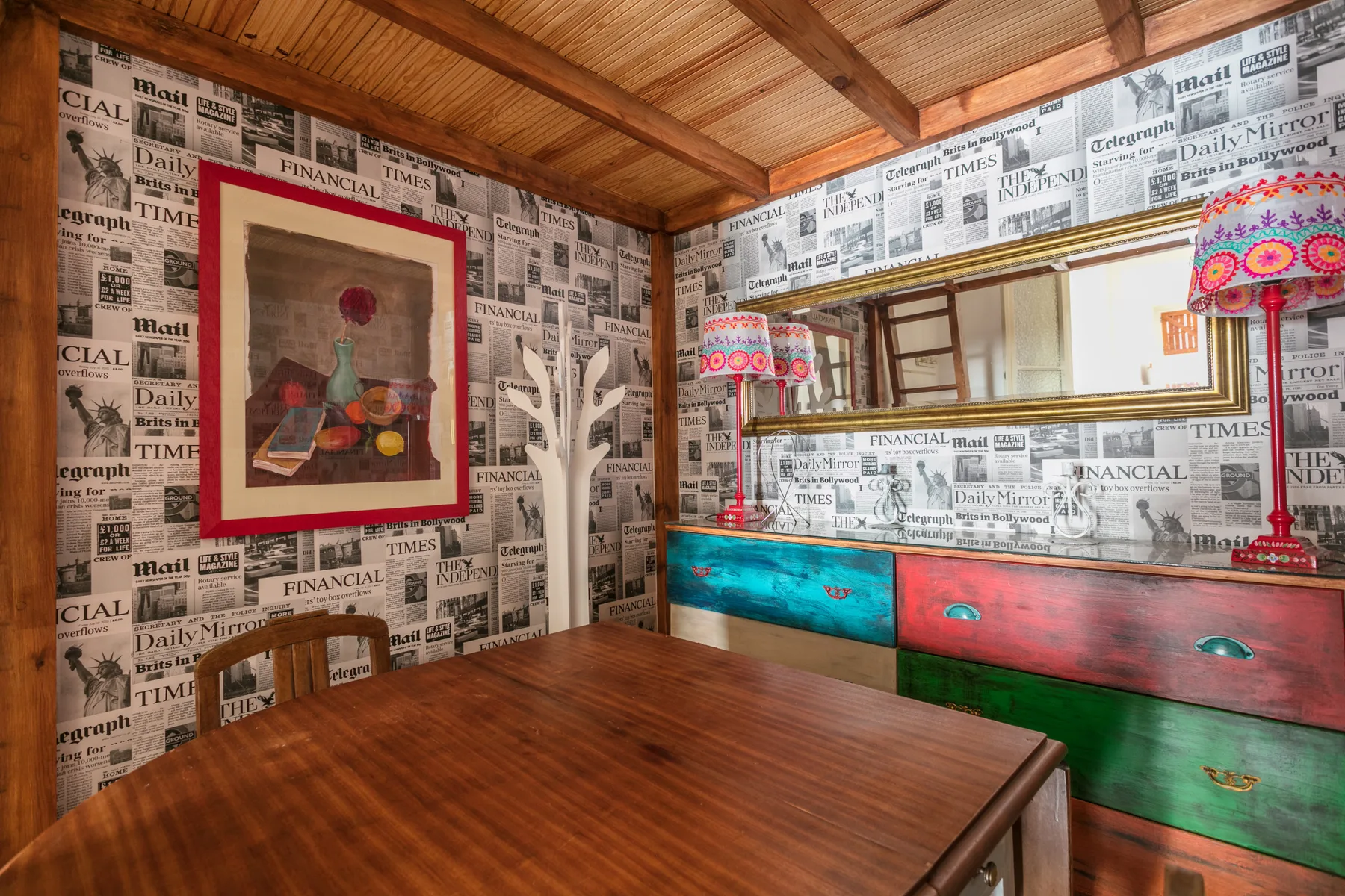 A dining area with a wooden table and newspaper-print wallpaper.