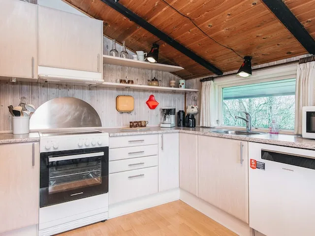 A bright kitchen with white cabinets, a stove, and a window above the sink.