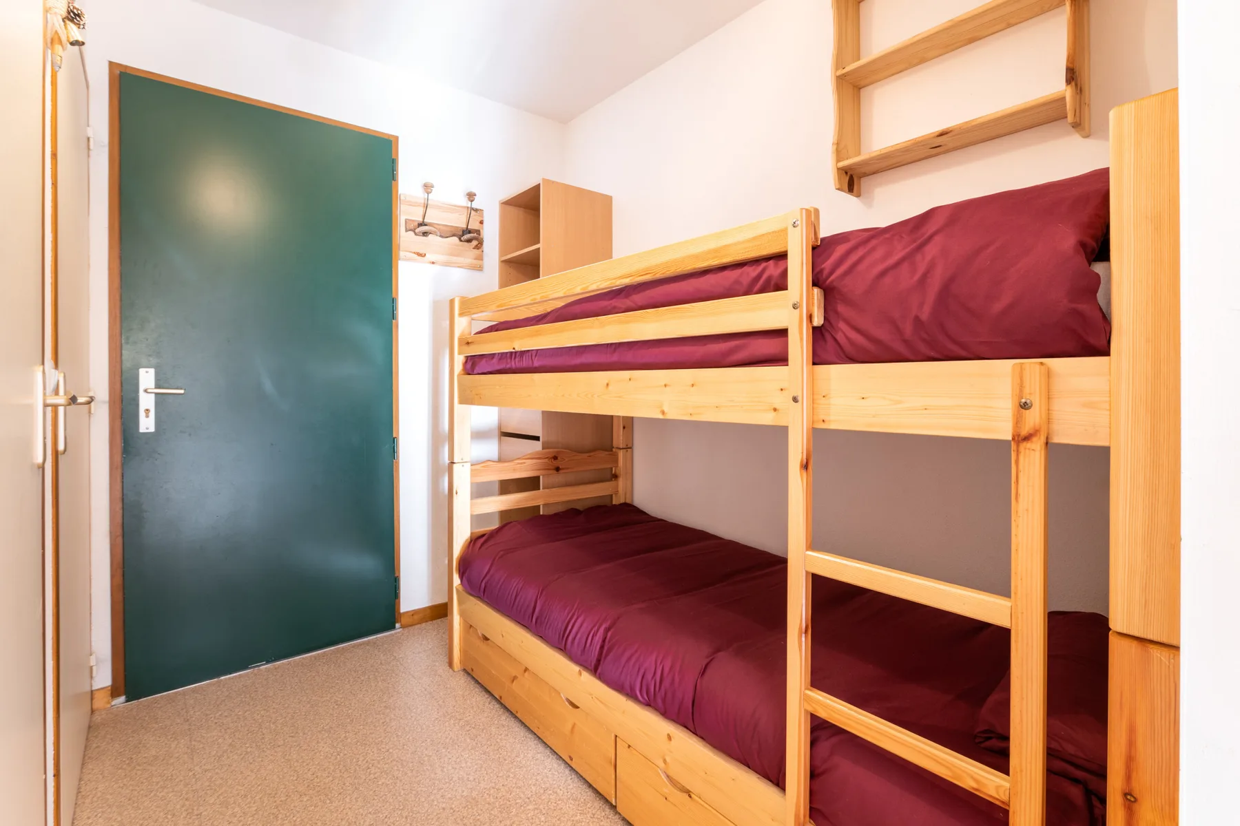 A bunk bed with burgundy bedding fills this compact bedroom.