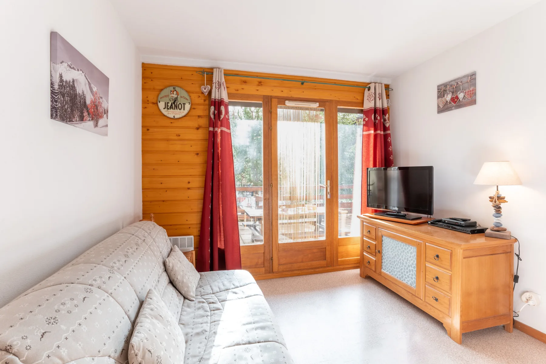 A bright living room with a sofa and wooden doors opening onto a balcony.