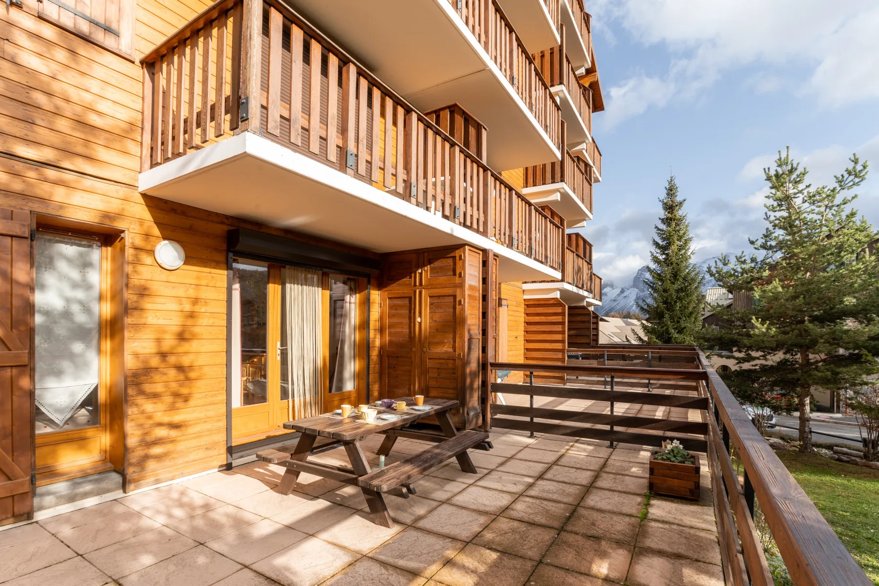 An outdoor terrace with a wooden picnic table beside a timber-clad building.
