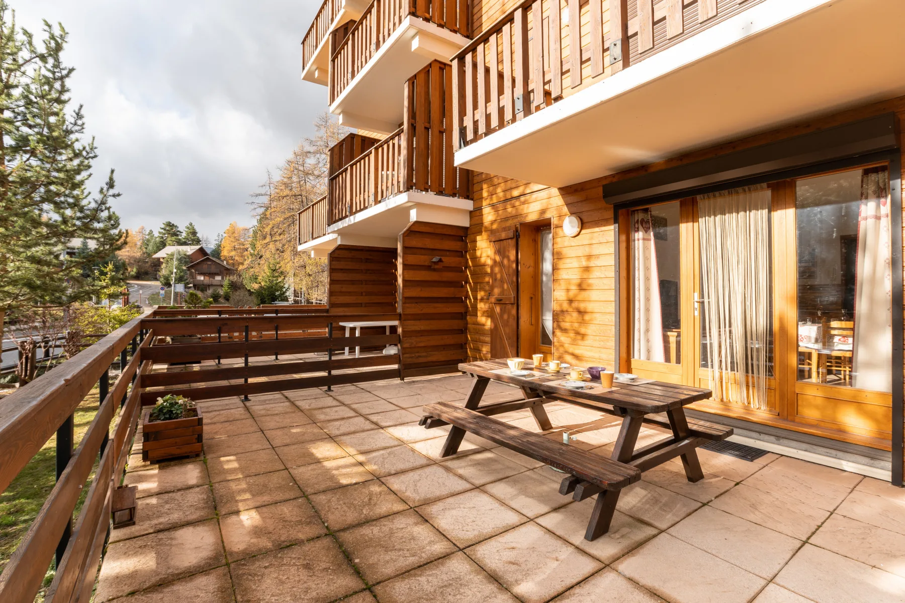 A wooden outdoor terrace with picnic-style seating beside a timber-clad building.