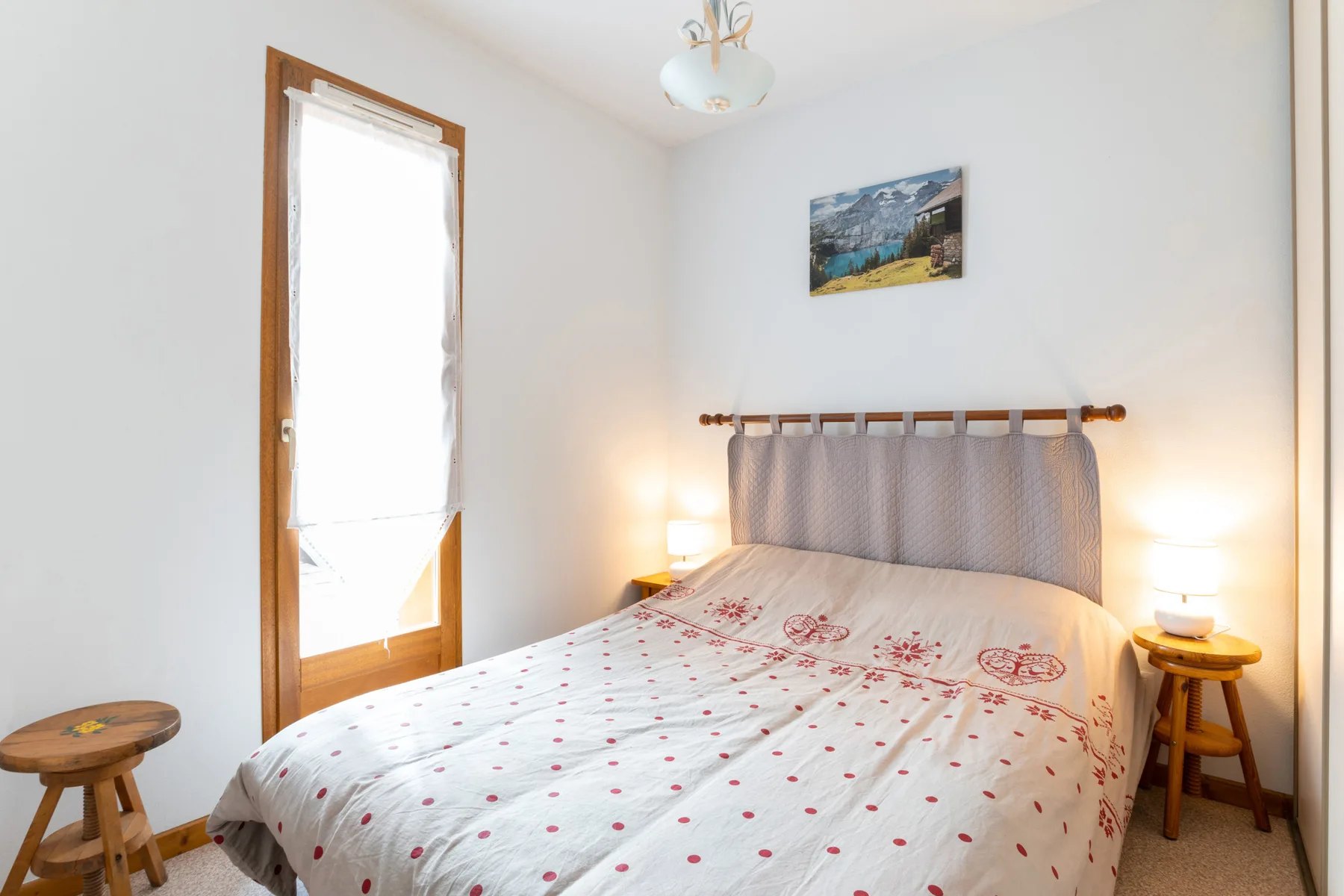 A bedroom with a bed beneath a curtained window.