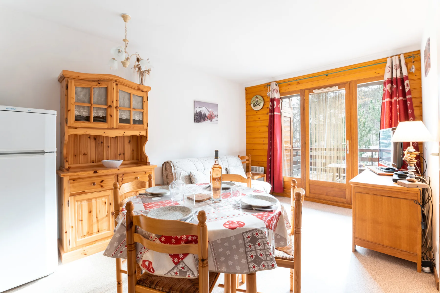 A dining area with a table beside a large window and red curtains.