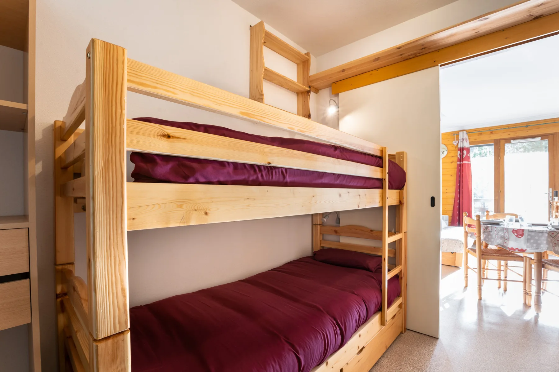 A bedroom with a wooden bunk bed and a doorway opening onto a dining area.