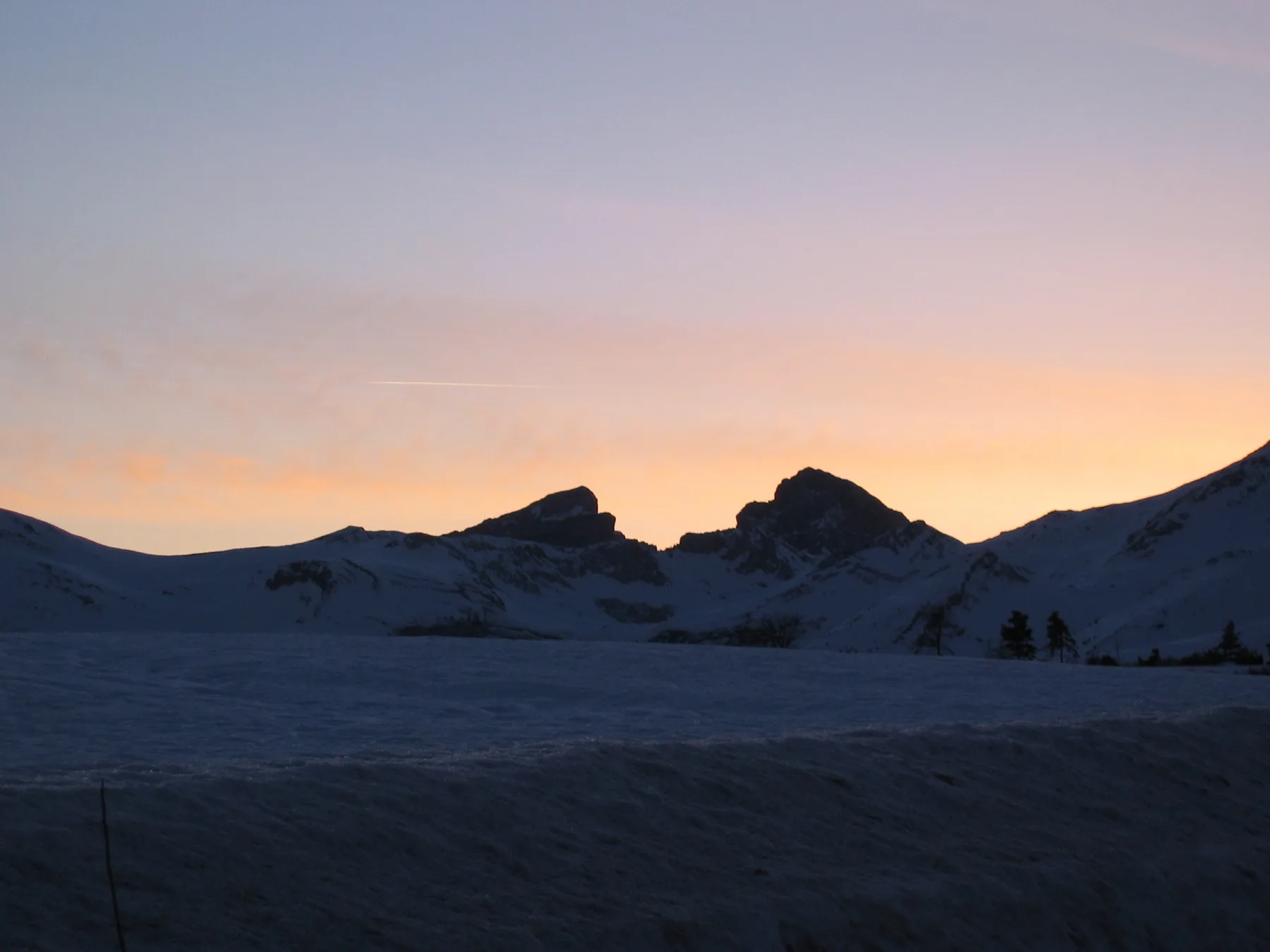 A snowy mountain landscape beneath a glowing sunset sky.