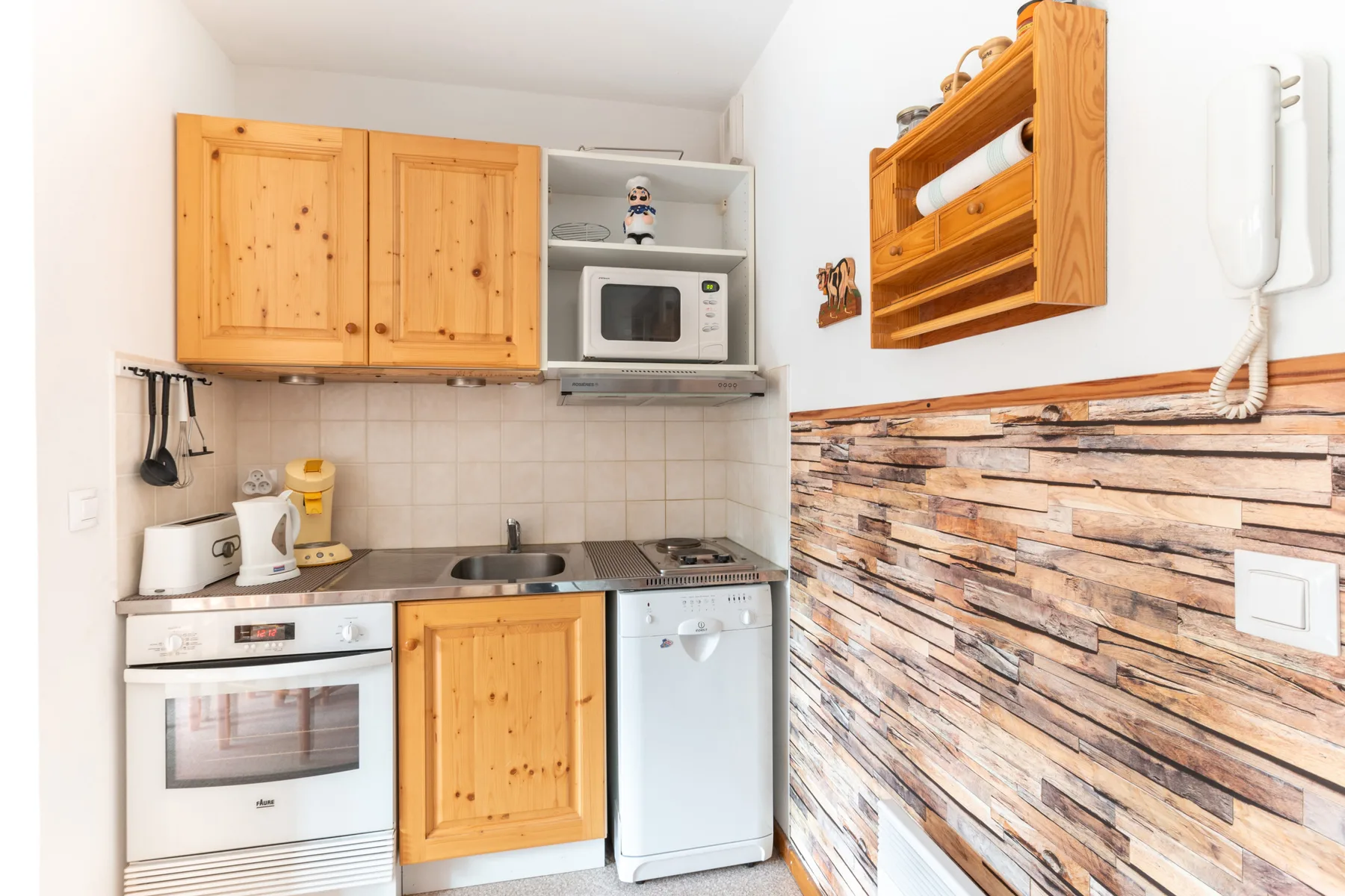 A compact kitchen with wooden cabinets, a stove, and a countertop microwave.