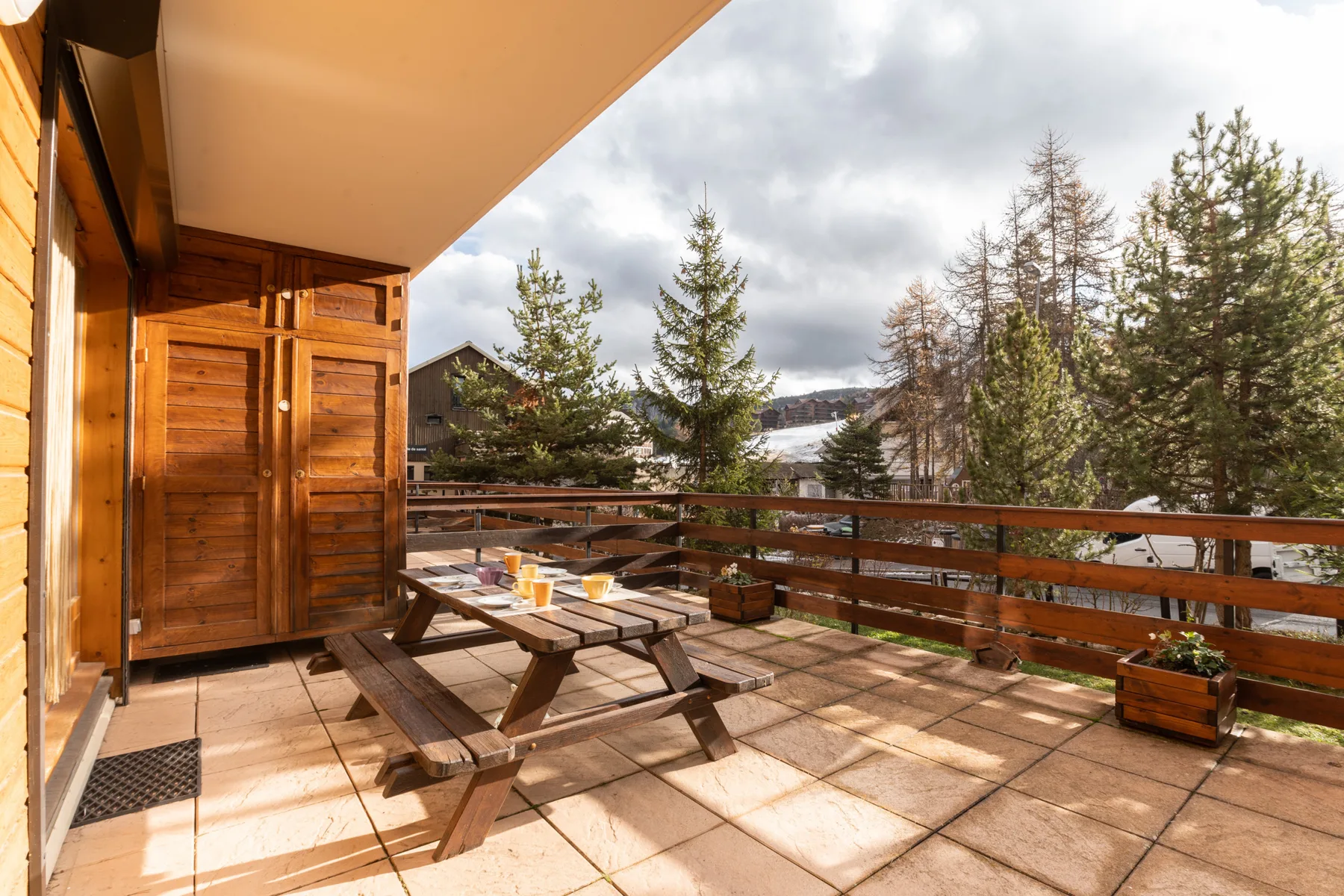 A wooden outdoor deck with picnic seating overlooks trees and a snowy landscape.