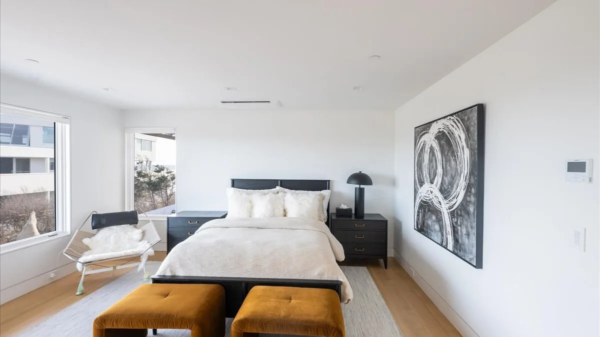 Un dormitorio luminoso con una cama bien arreglada y una gran obra abstracta en la pared.