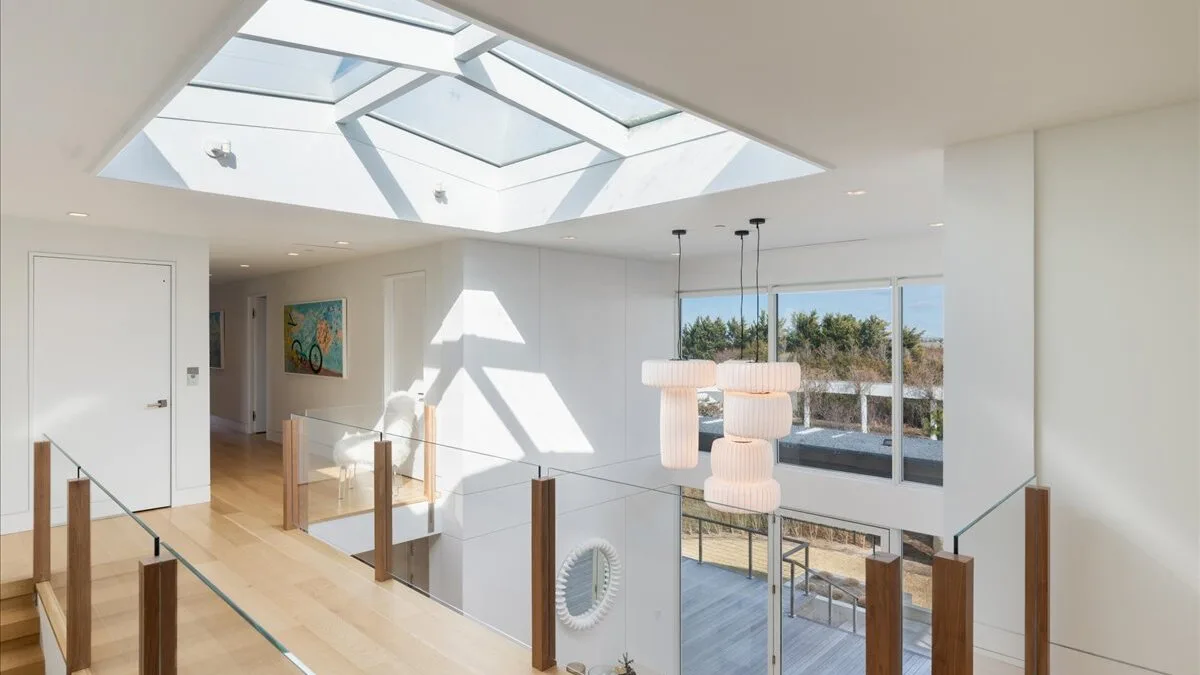 Un interior moderno y luminoso, con un tragaluz de vidrio y lámparas colgantes sobre la zona de estar.