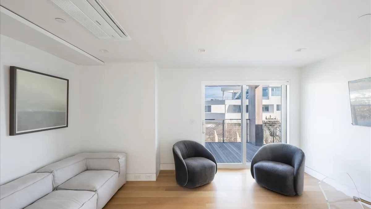 Una sala luminosa con dos sillones frente a las ventanas.