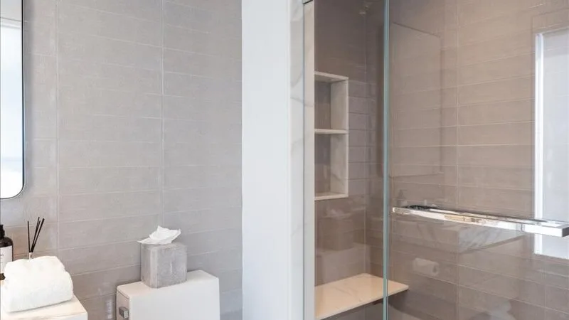 Un baño con azulejos, una ducha de vidrio y un pequeño estante en la pared.