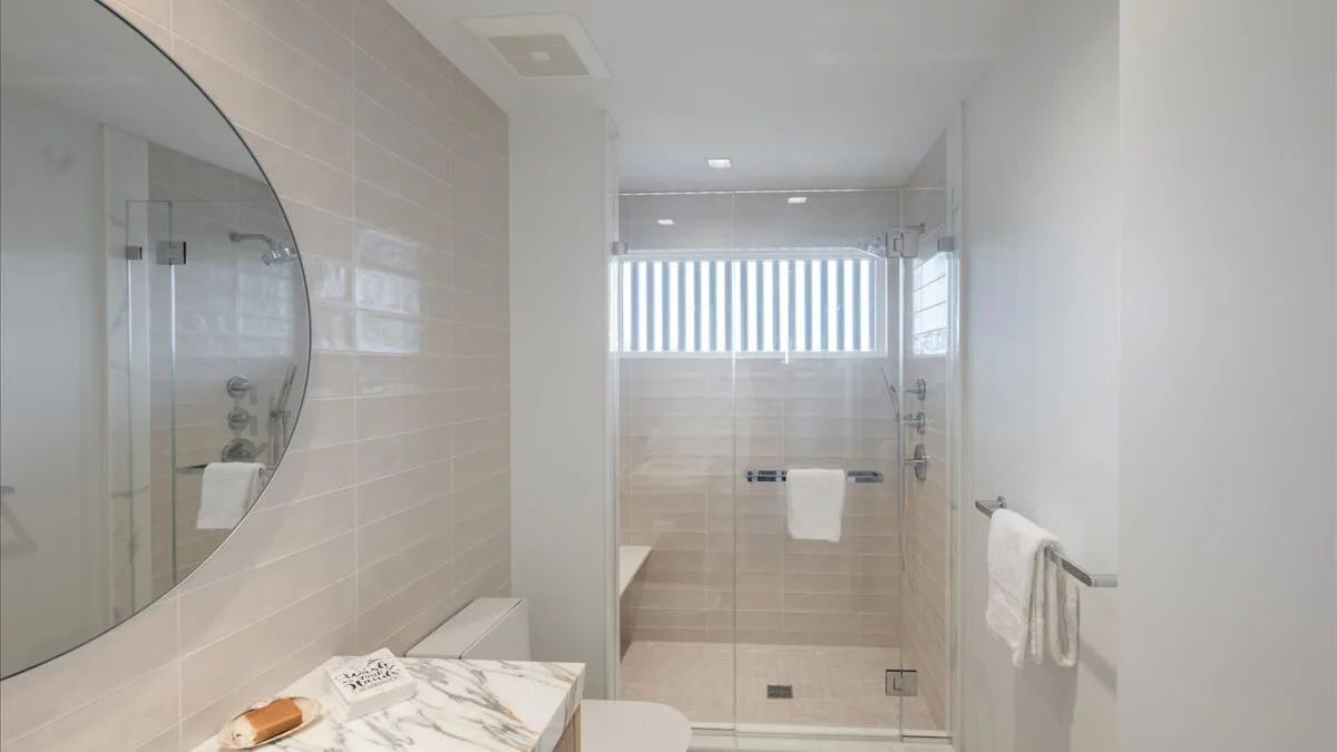 Un baño luminoso con azulejos, una ducha de vidrio y un lavabo.