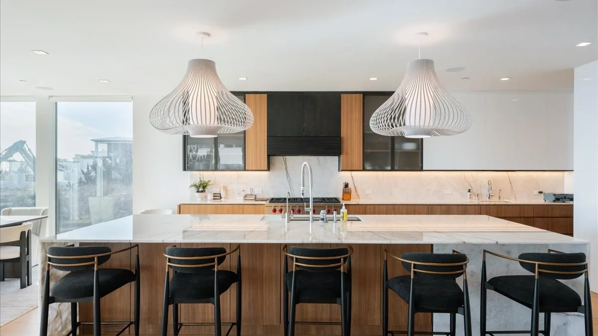 Una cocina moderna y luminosa con una isla larga y lámparas colgantes.