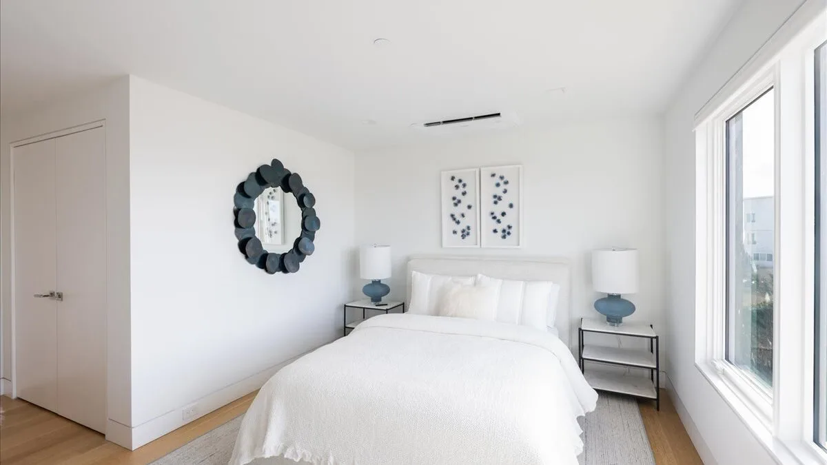 Un dormitorio luminoso con una cama blanca y grandes ventanas.
