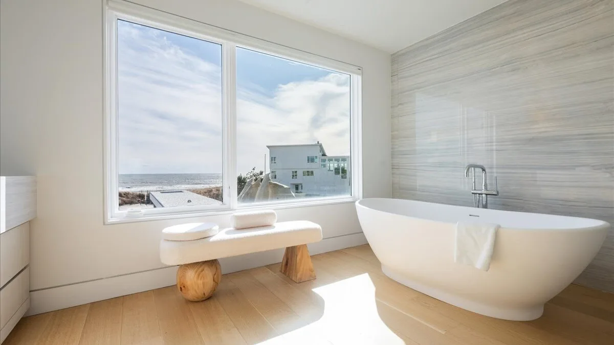 Un baño luminoso con una bañera exenta junto a grandes ventanas.