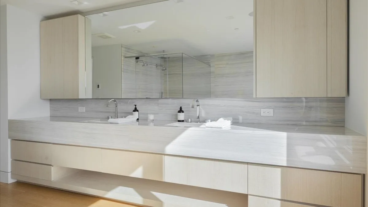 Un tocador de baño con dos lavabos está bajo un espejo amplio.