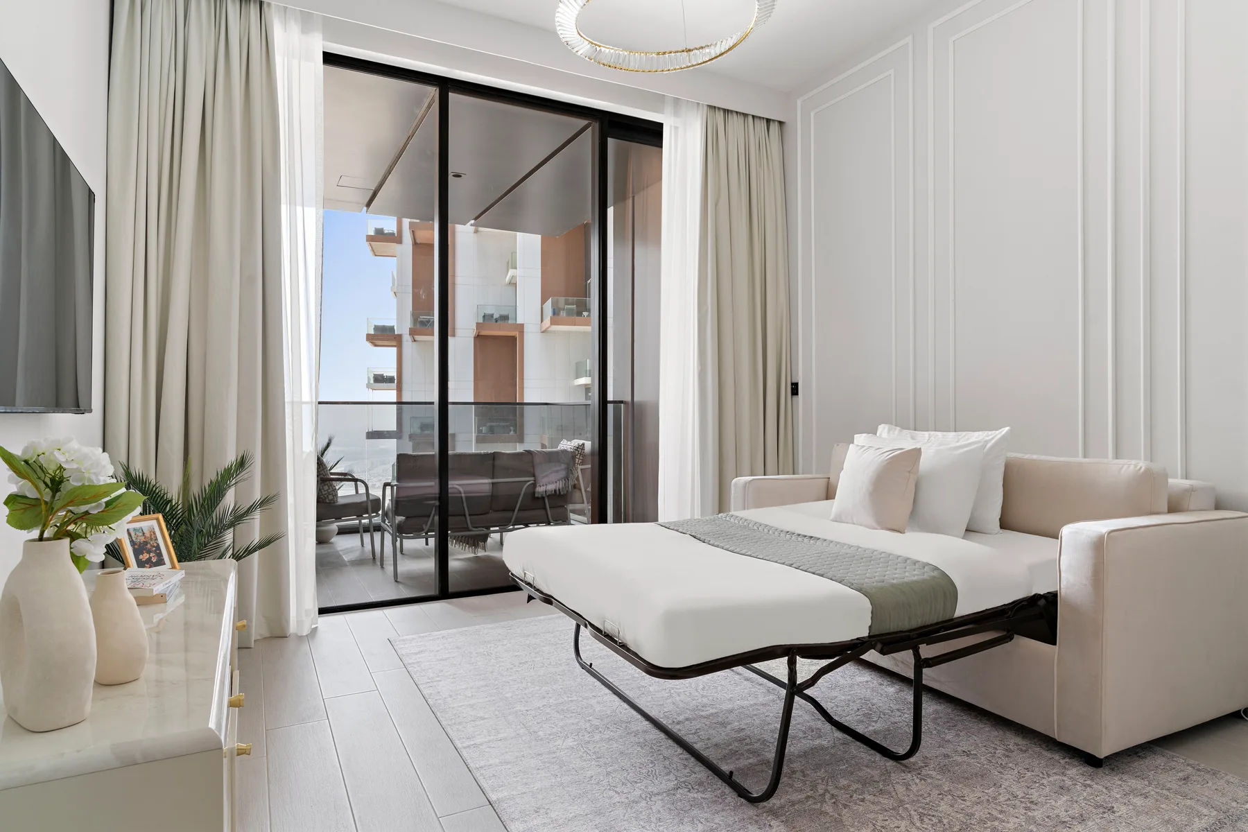 A bedroom with a neatly made bed beside large glass doors opening onto a balcony.