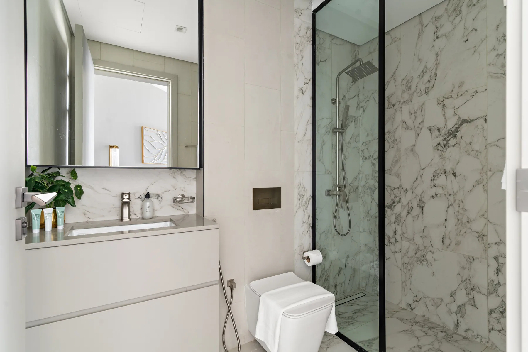 A modern bathroom with a vanity, wall mirror, toilet, and glass shower.