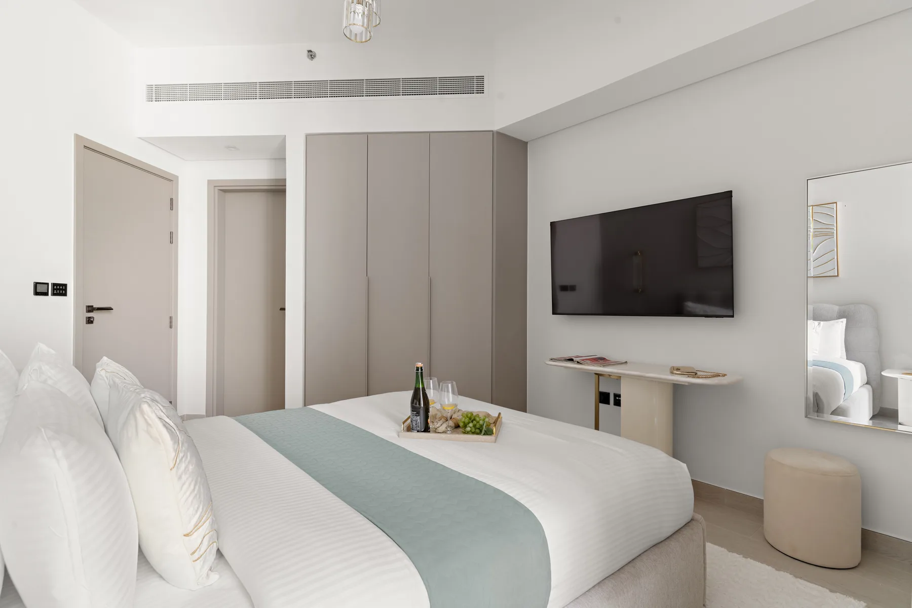 A bright bedroom with a neatly made bed and a wall-mounted television.