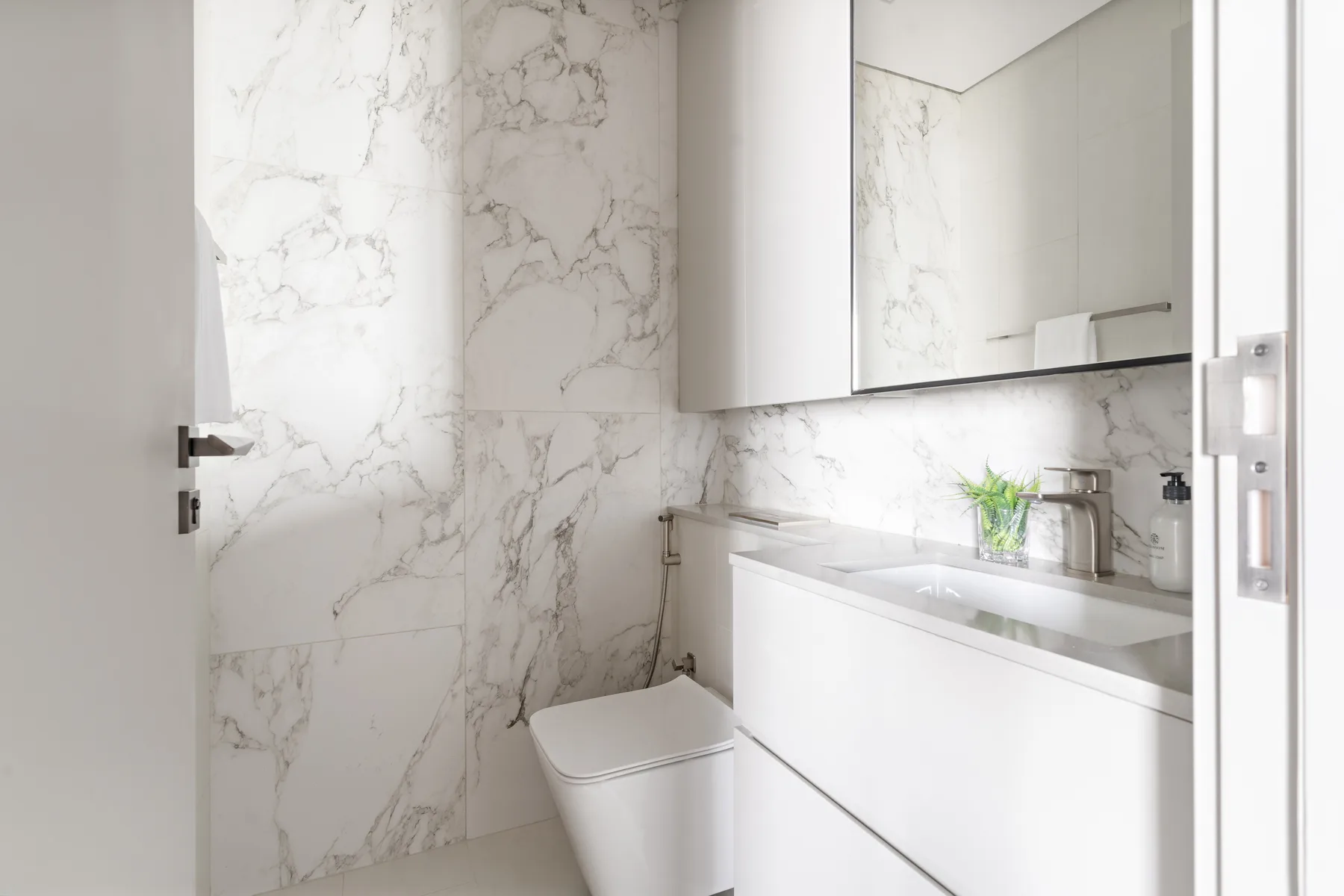A bright bathroom with a white sink vanity and marble-patterned walls.