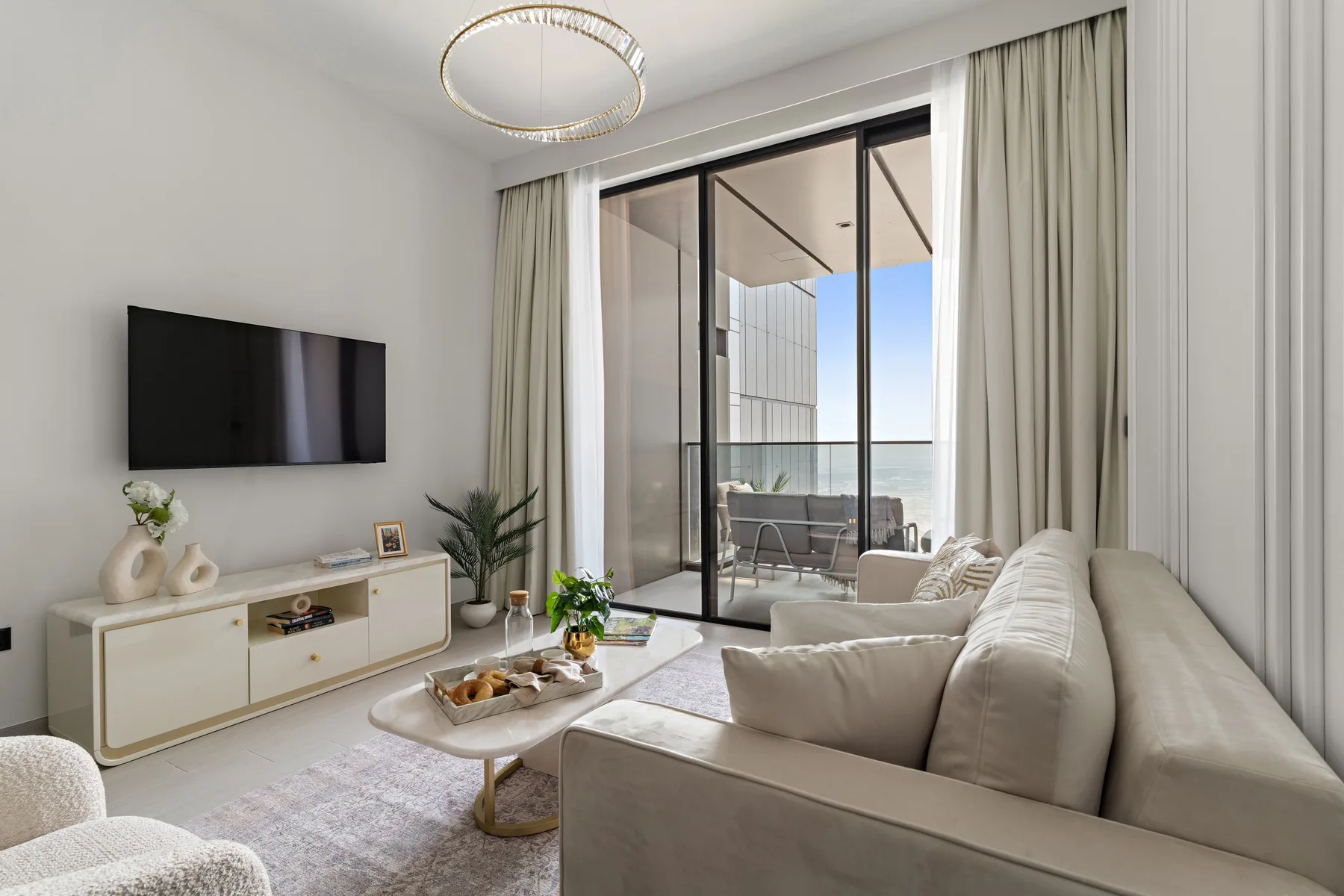 A bright living room with neutral seating and sliding glass doors opening onto a balcony.