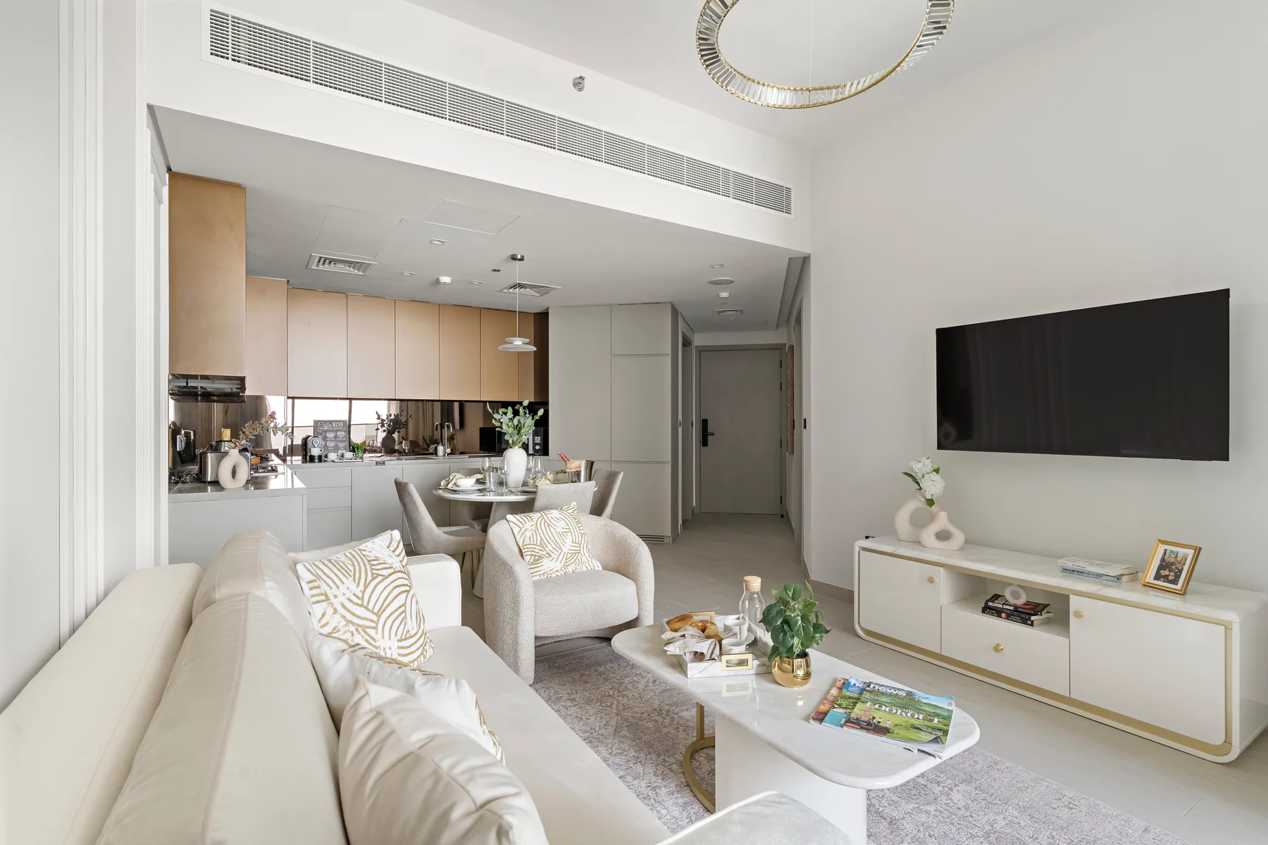 A bright living room opens onto a kitchen, with seating and a wall-mounted television.