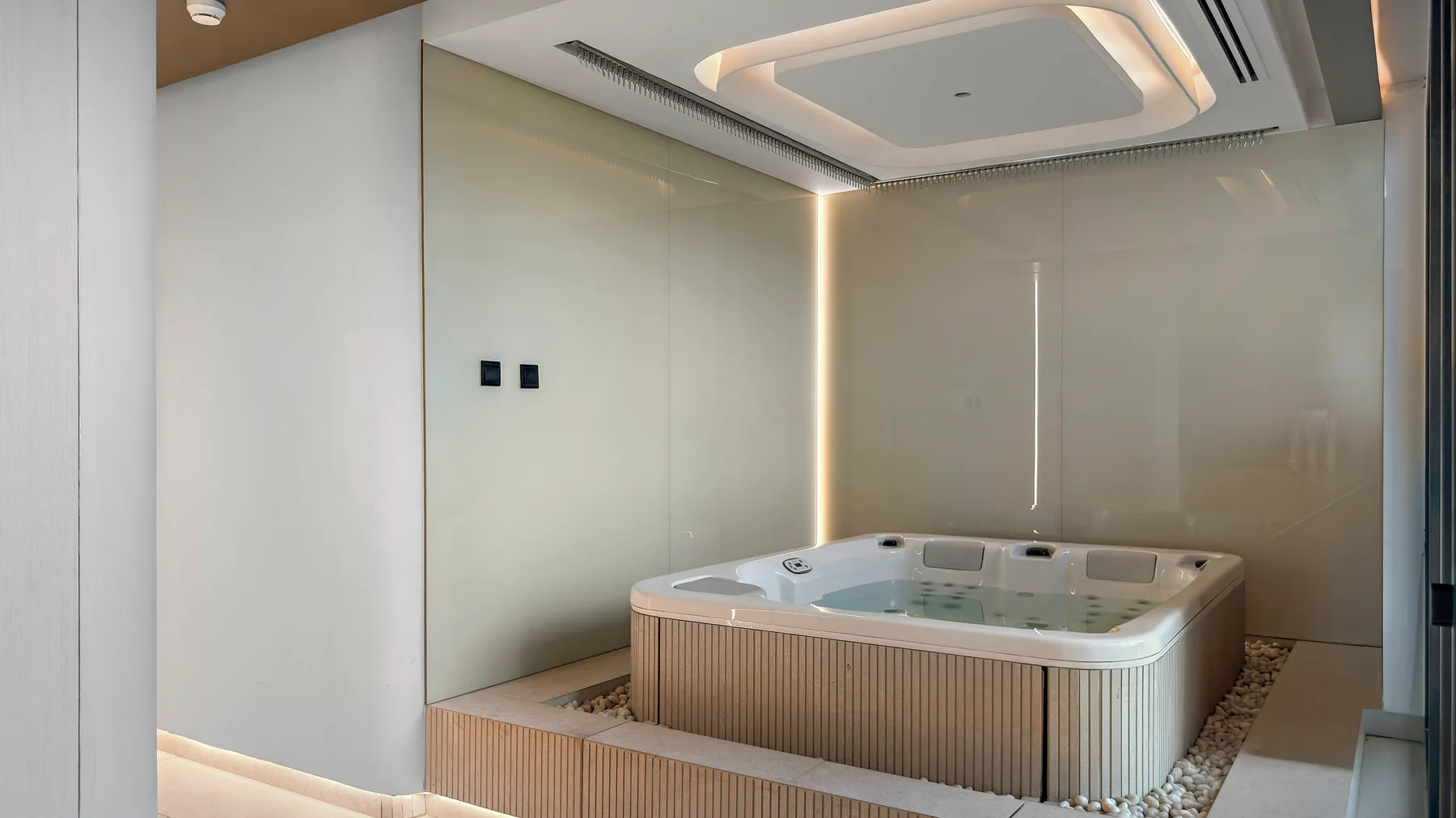 A modern indoor spa area features a large hot tub set into a raised platform.