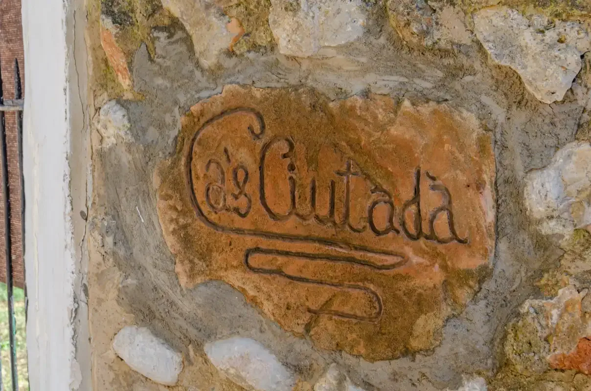 A carved name plaque is set into a rough stone wall beside a window.