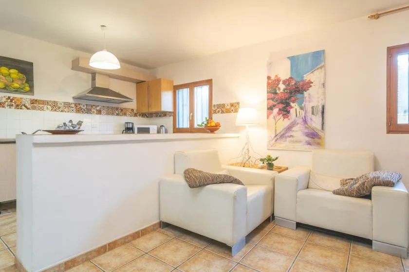 A living area with light-colored seating faces an open kitchen with a breakfast counter.