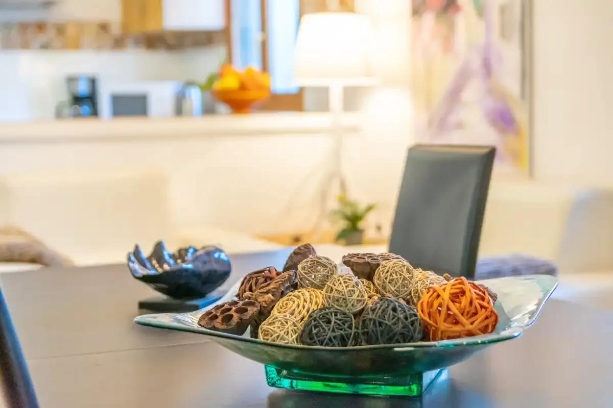 A dining table displays a glass bowl filled with decorative woven spheres.