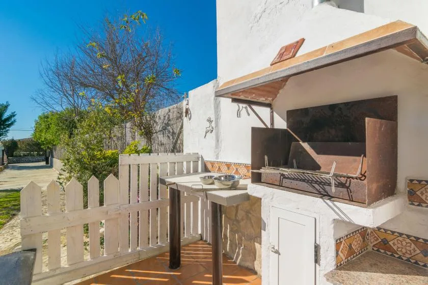 A sunny outdoor patio with a built-in barbecue and a small fenced seating area.