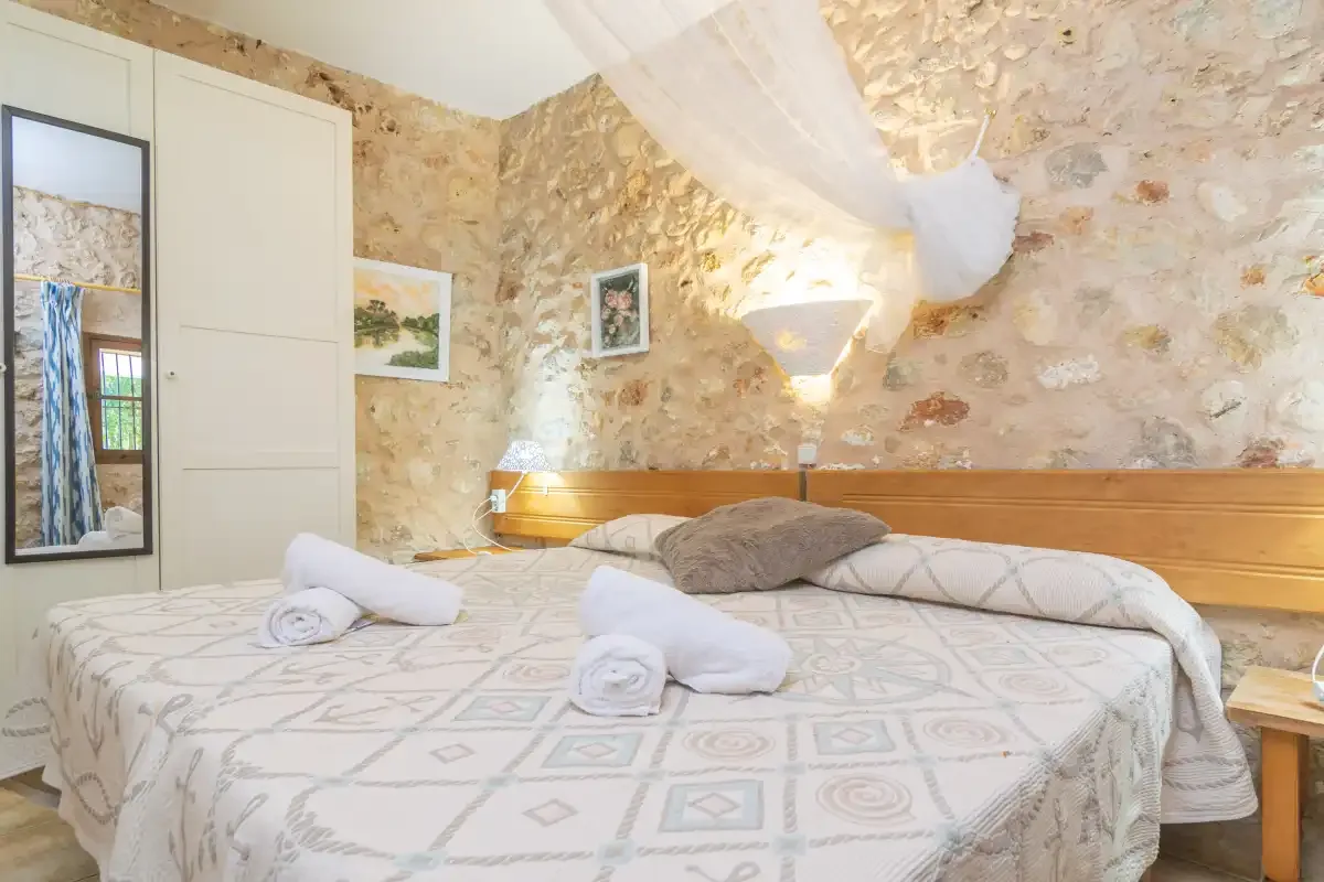 A bedroom with a patterned bedspread and exposed stone walls.