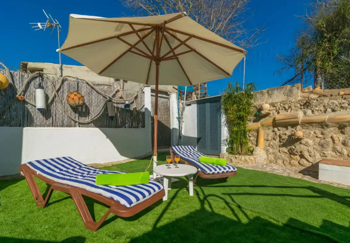 An outdoor patio has striped loungers beneath a large umbrella.