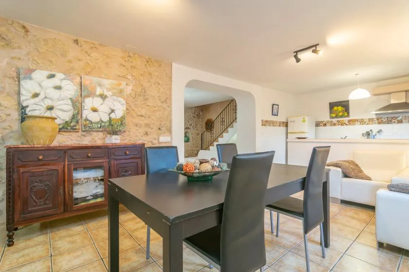 A dining area with a dark table and chairs beside a kitchen and staircase.