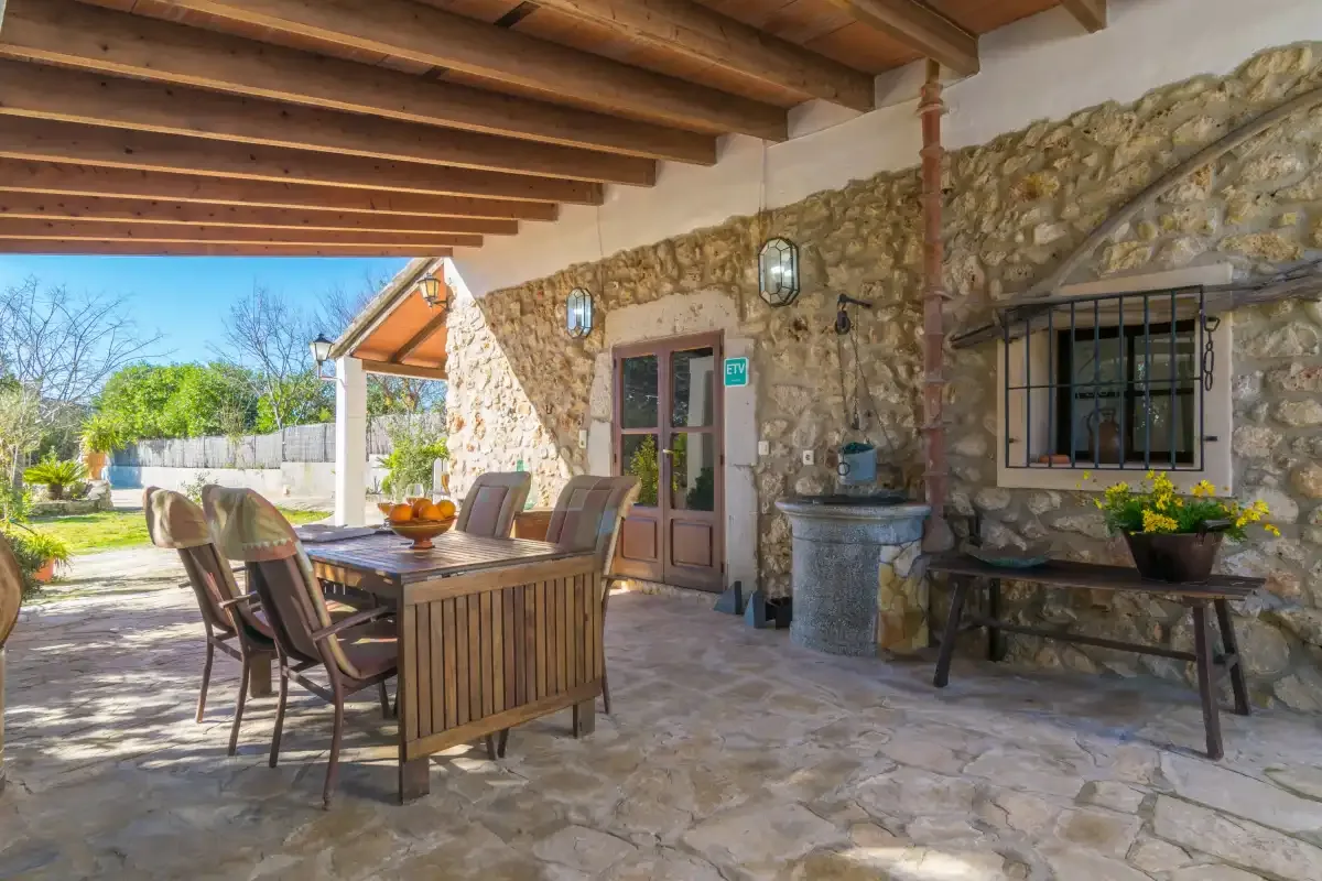 A stone patio with an outdoor dining table beneath a wooden-beam roof.